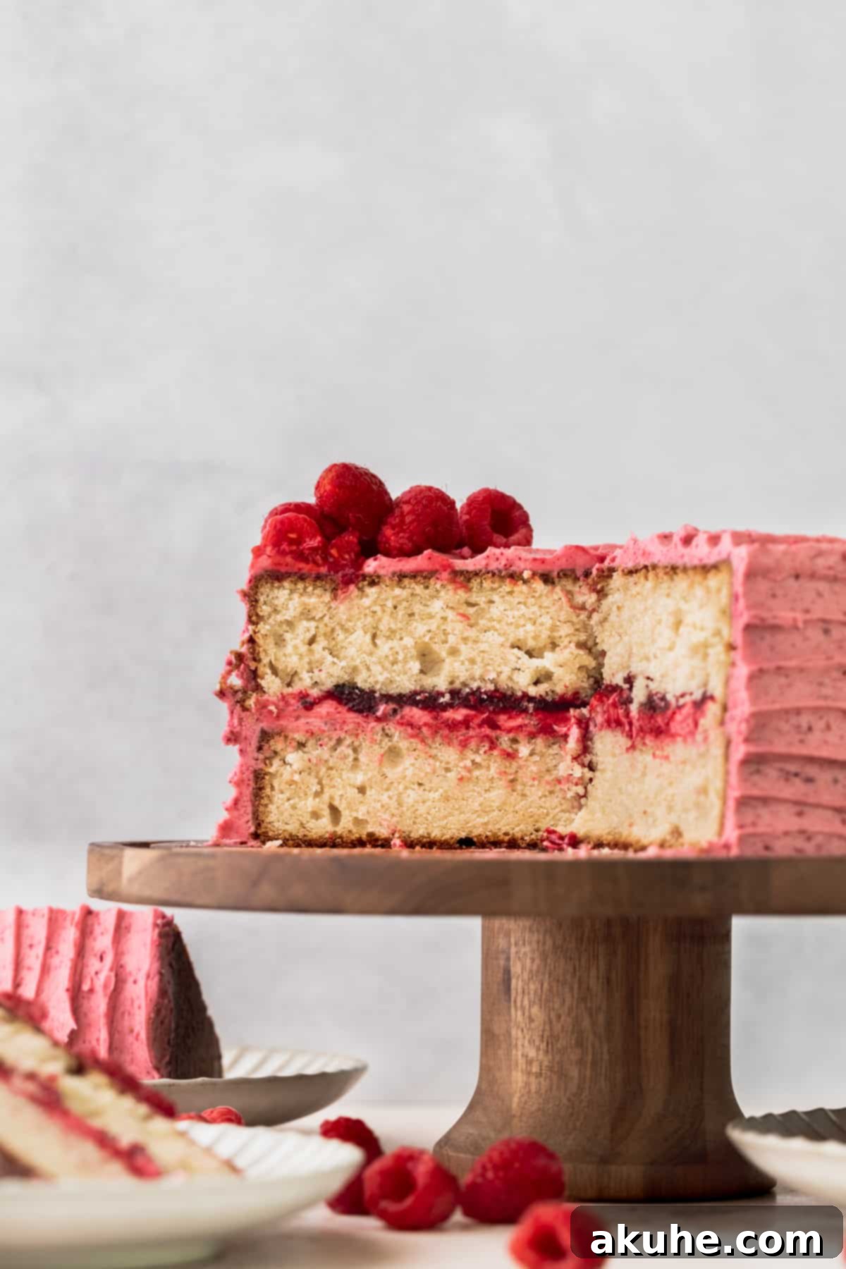 A beautifully decorated two-tier vanilla raspberry cake displayed on an elegant cake stand, showcasing the smooth raspberry cream cheese frosting and a delicate topping of fresh raspberries.
