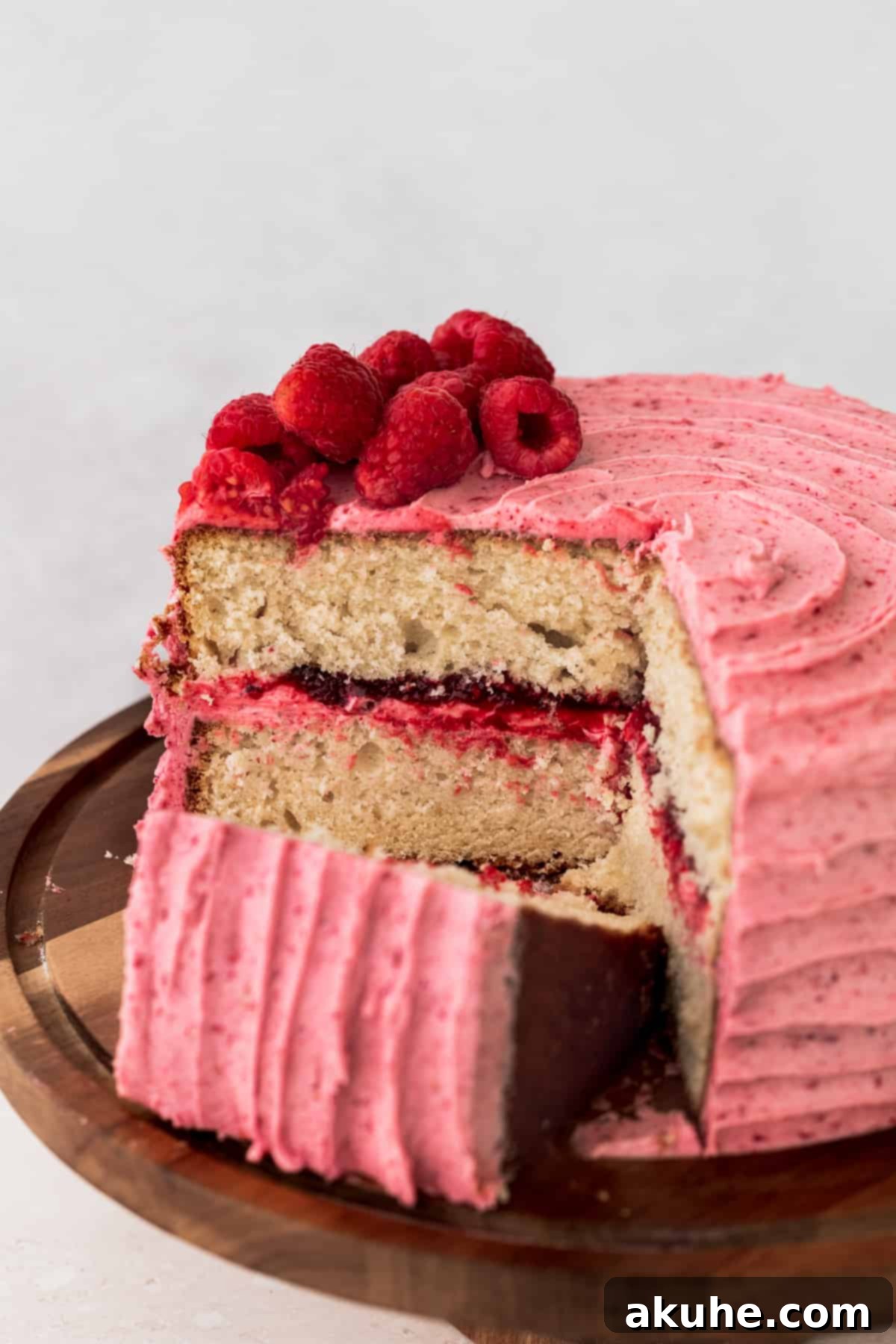 A cross-section of the vanilla raspberry cake, revealing perfectly even layers of vanilla cake, a thick spread of seedless raspberry jam, and generous frosting between the layers.