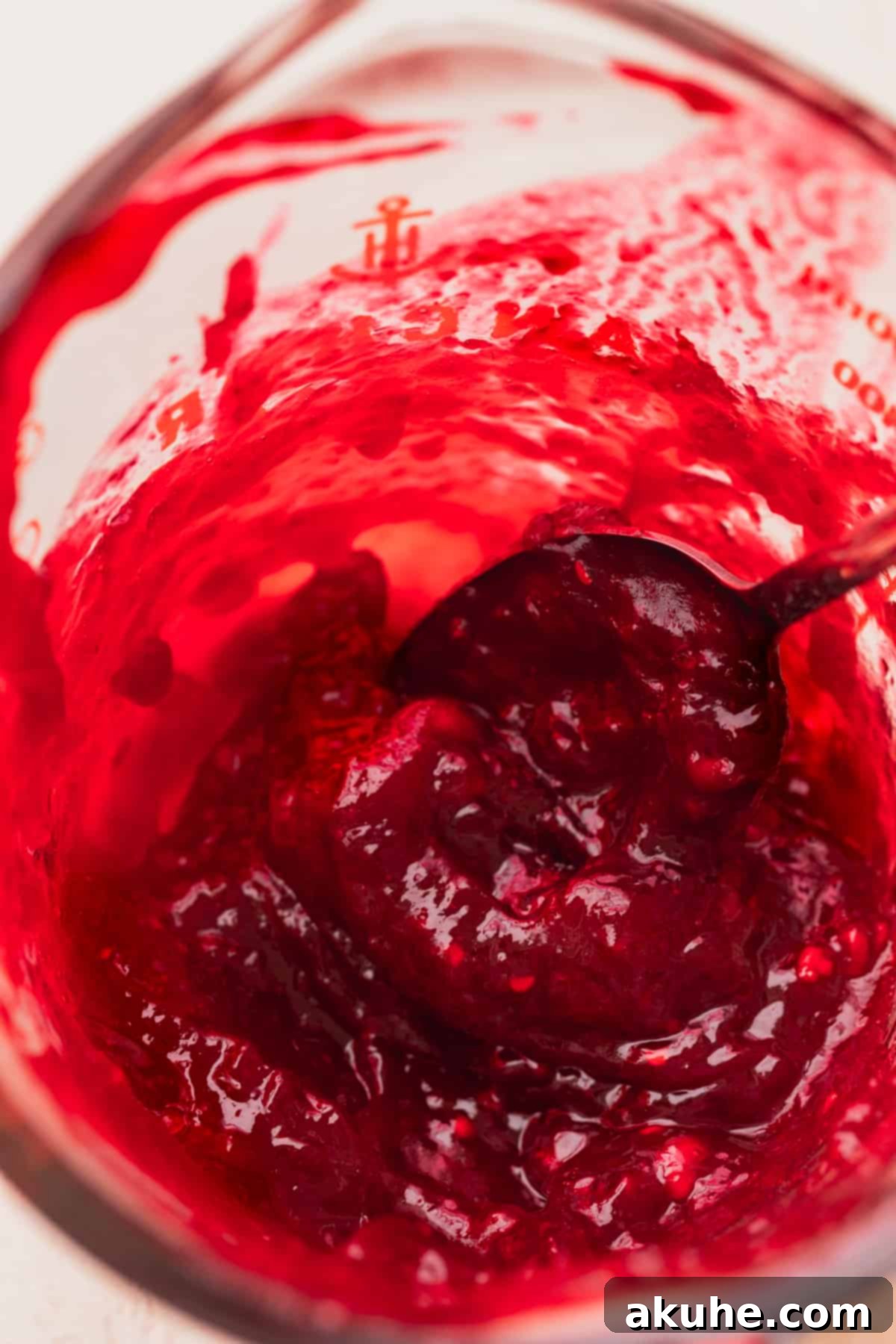 Vibrant, homemade raspberry jam cooling in a clear glass measuring cup, ready to be layered within the cake.