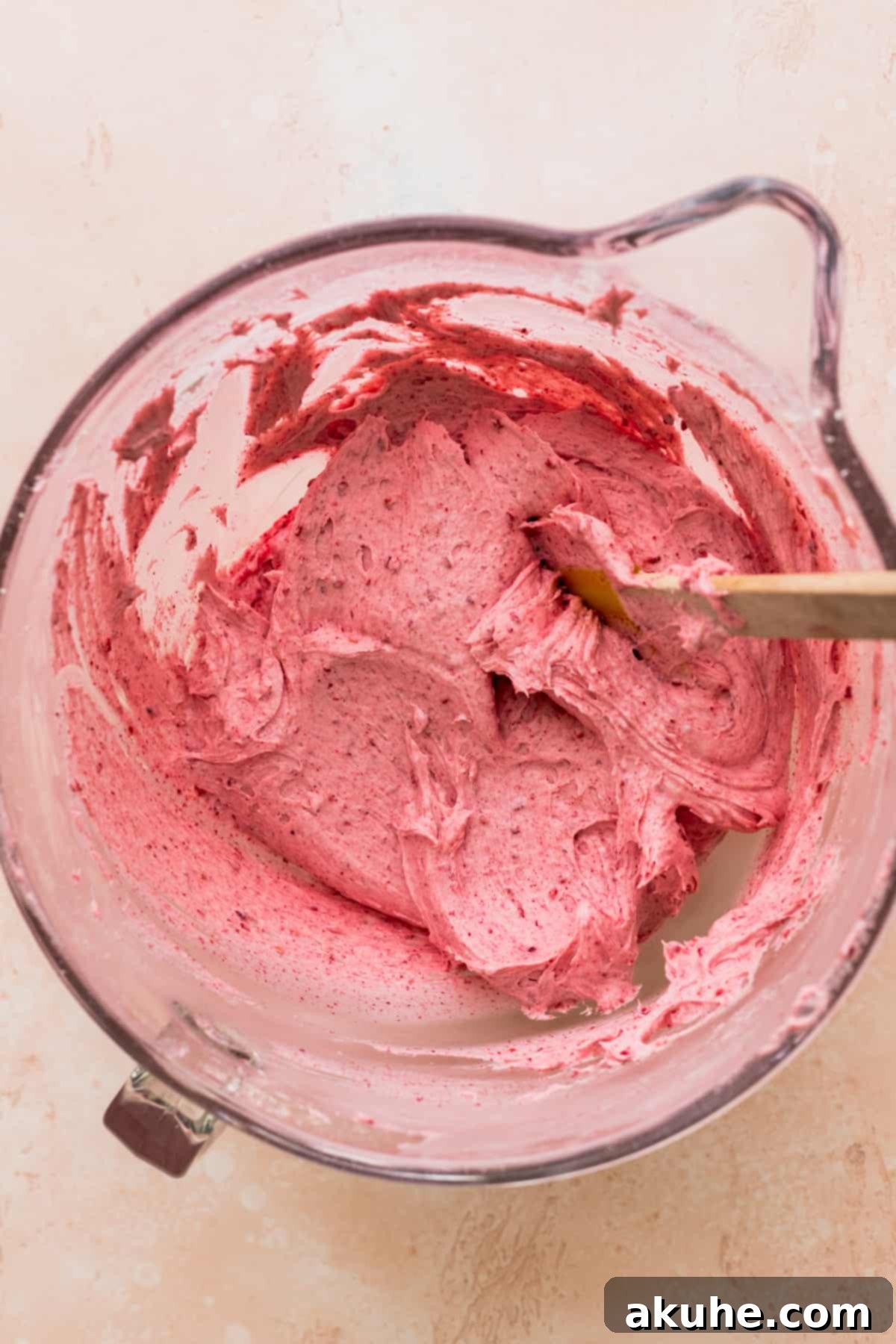 Fluffy, pink raspberry cream cheese frosting resting in a glass bowl, showcasing its smooth texture and rich color.