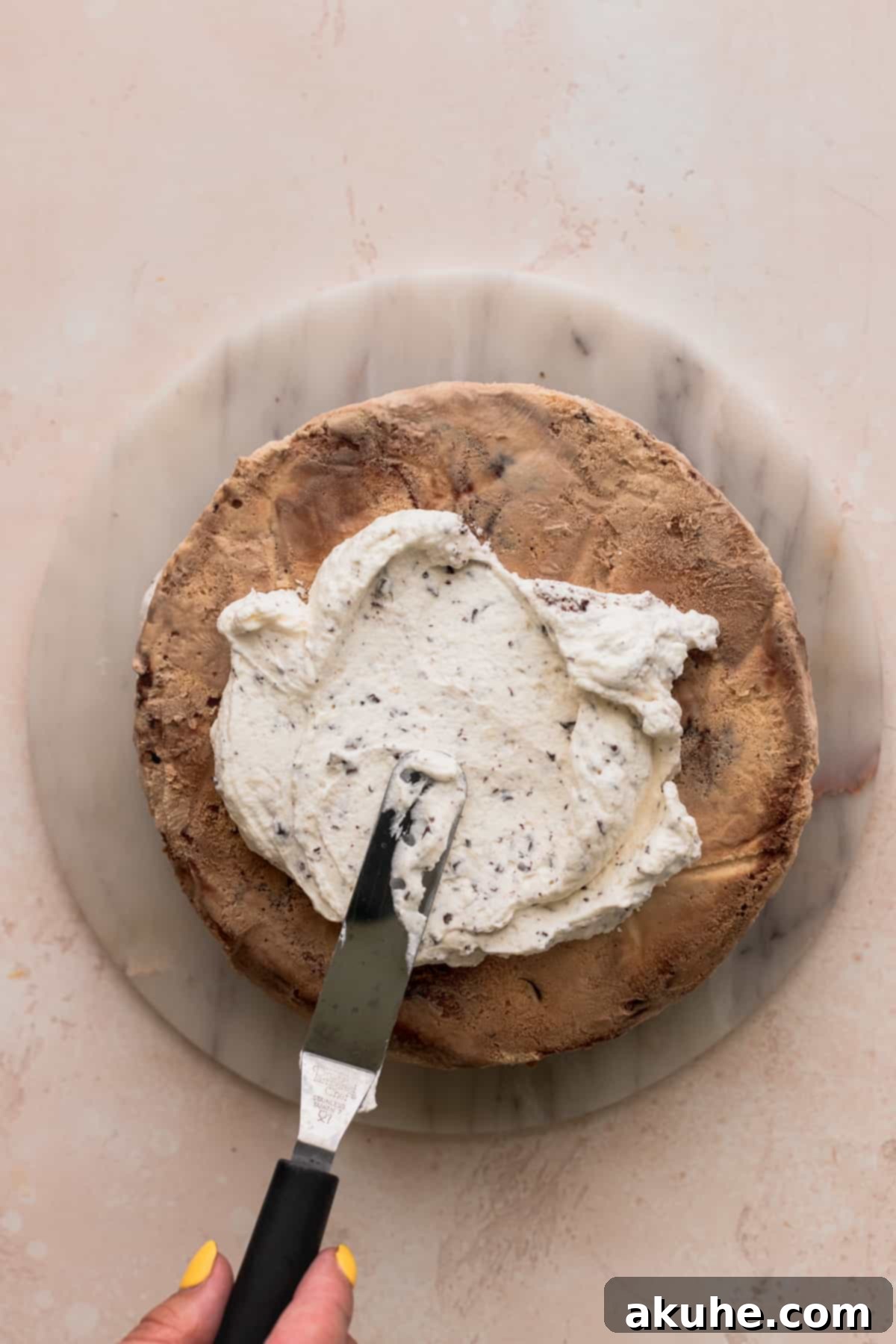 Ultimate Cookie Dough Ice Cream Cake 14 The process of spreading whipped cream onto the top layer of the assembled cookie dough ice cream cake.