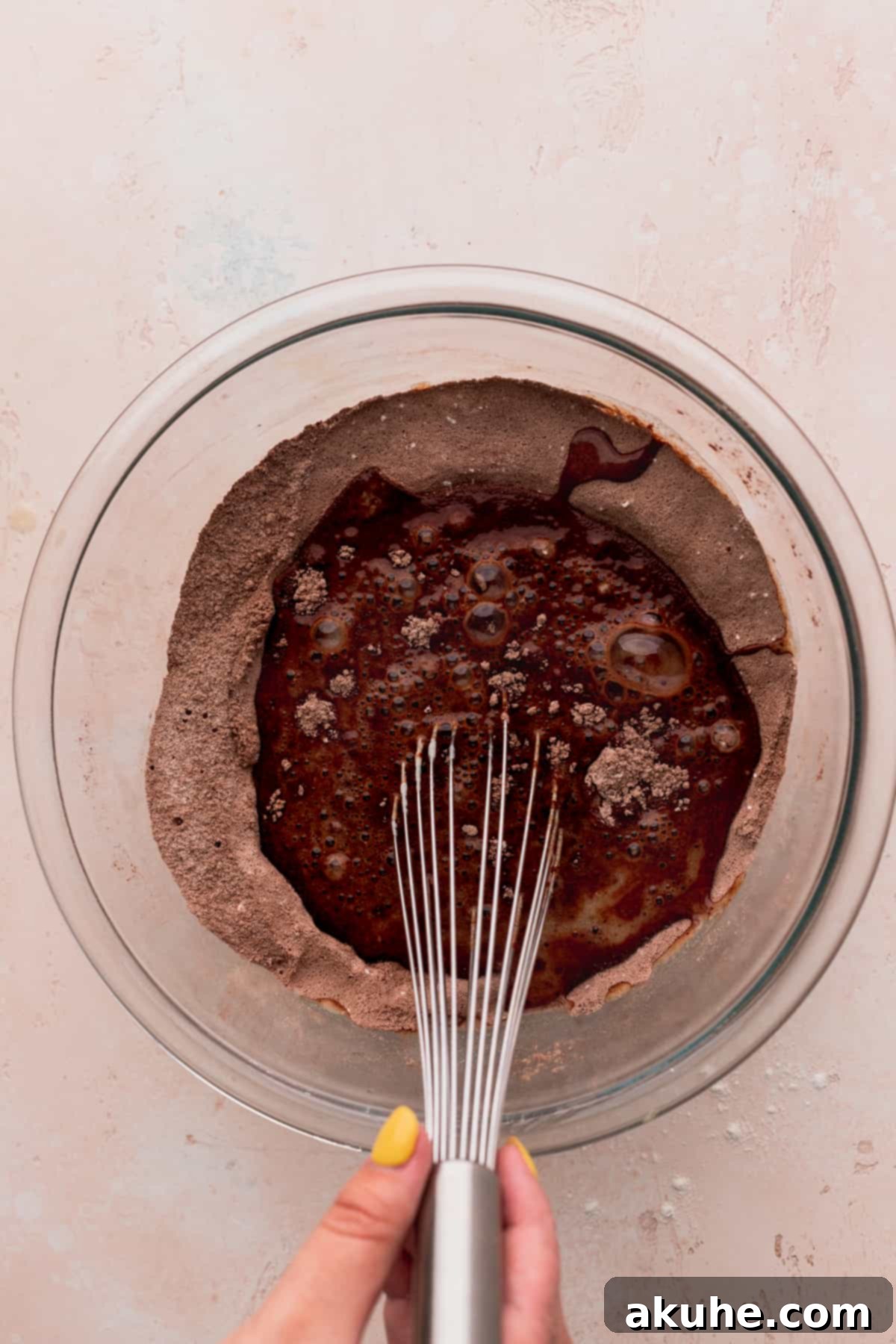 Ultimate Cookie Dough Ice Cream Cake 5 Wet ingredients being carefully added on top of dry ingredients in a clear glass mixing bowl.