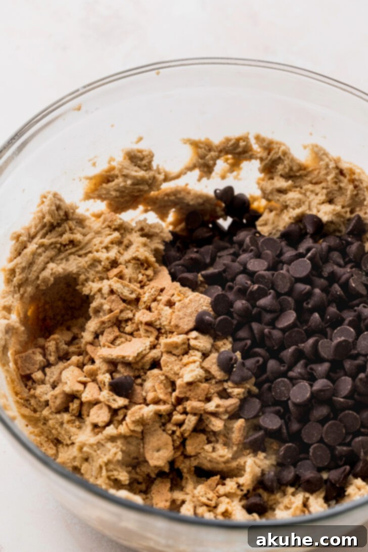 Gooey S'mores Cookies 5 Cookie dough in a bowl, with graham cracker pieces and chocolate chips scattered on top, ready to be mixed in.