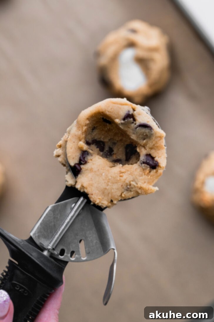 Gooey S'mores Cookies 7 A scoop of cookie dough with a thumb pressed into the center, creating a perfect cavity for the marshmallow.