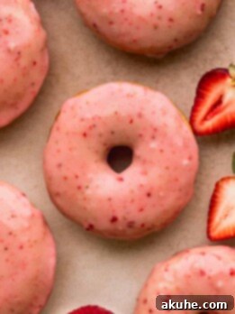 Glazed Strawberry Treats 12 Close up of strawberry glazed donuts with strawberries on the side.