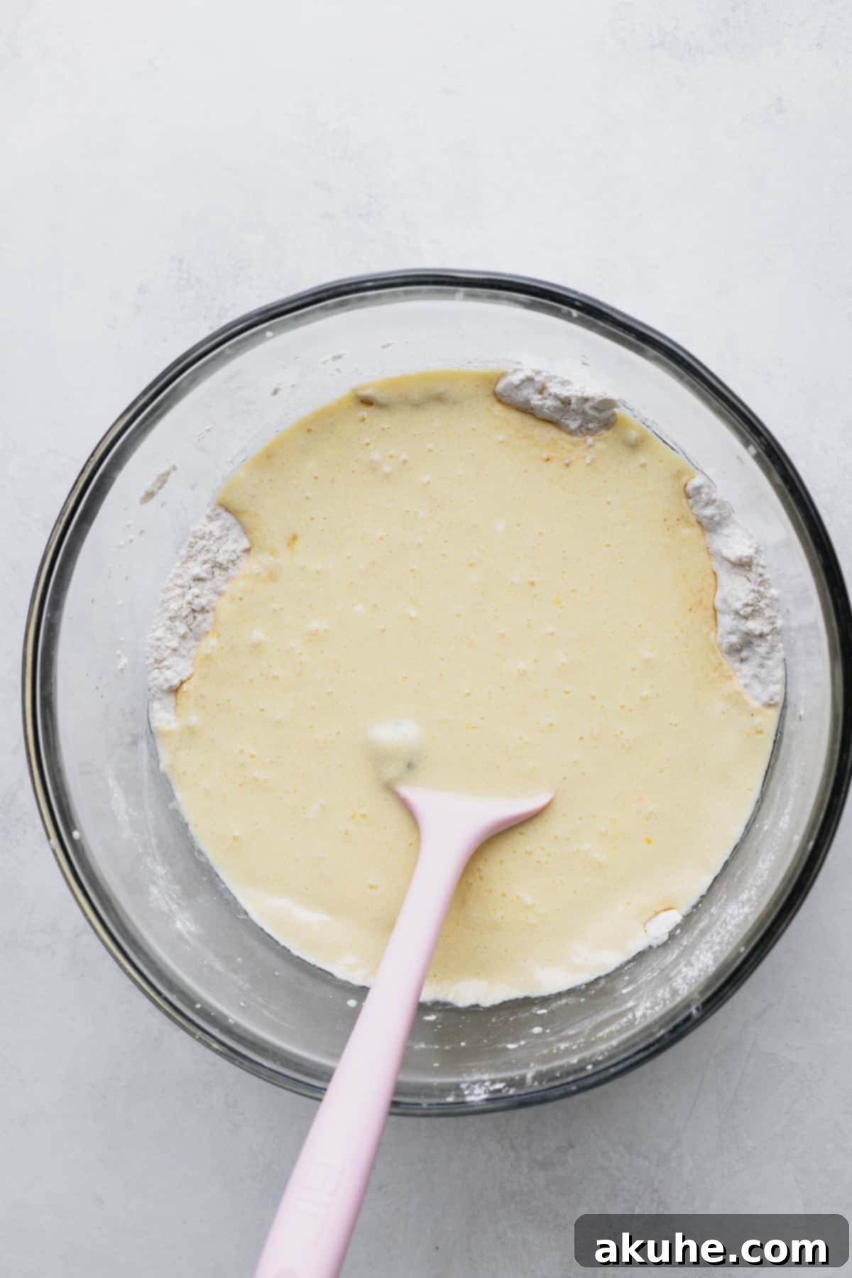 Ultimate Blueberry Chocolate Chip Muffins 4 Wet ingredients freshly added to the dry flour mixture in a glass bowl, before being fully combined.