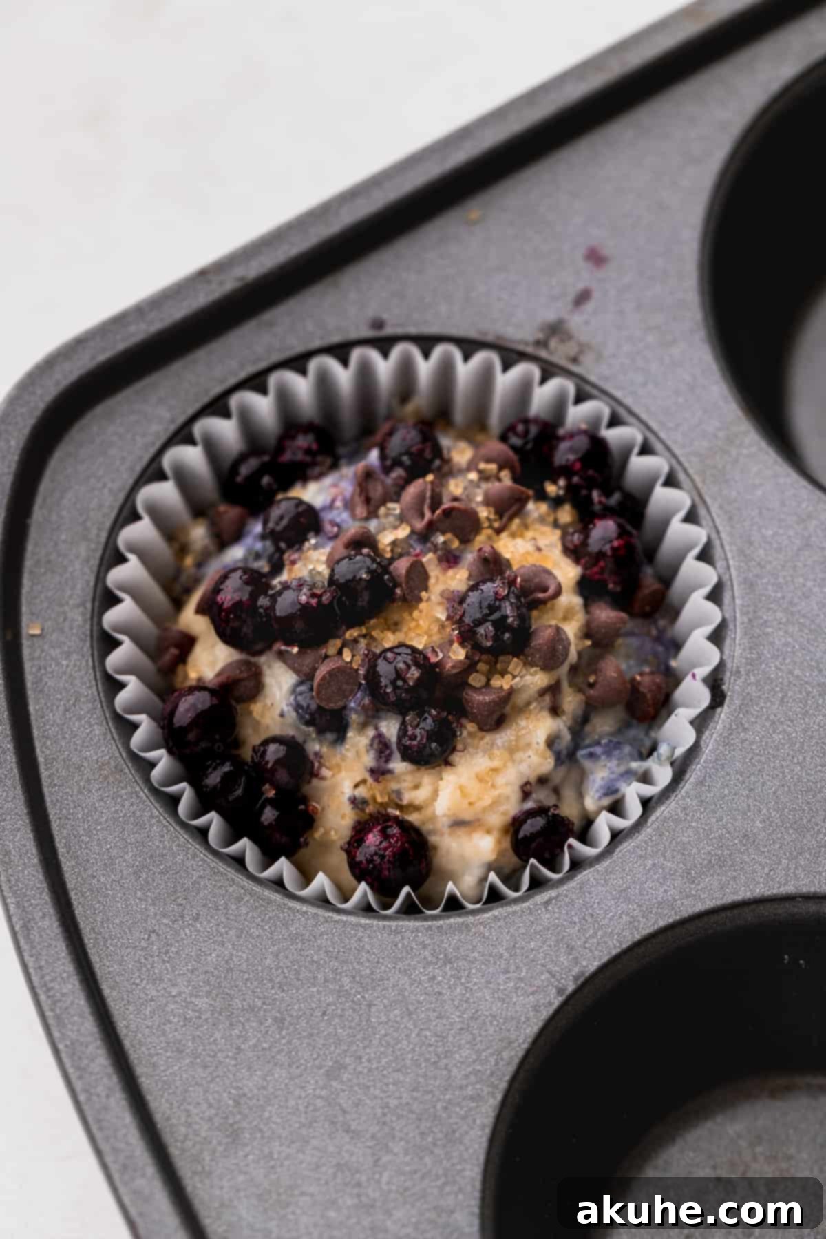 Ultimate Blueberry Chocolate Chip Muffins 7 A perfectly portioned scoop of muffin batter nestled within a paper liner in a muffin tin, ready for topping and baking.