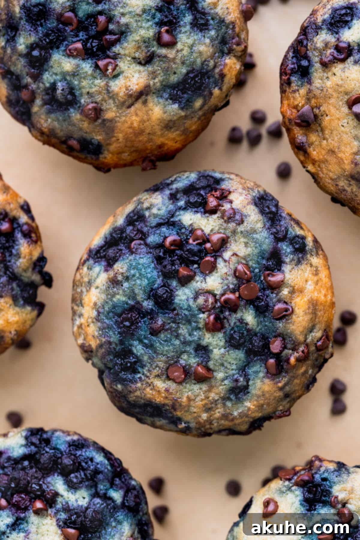 Ultimate Blueberry Chocolate Chip Muffins 8 Close-up view of the golden, crusted tops of freshly baked blueberry chocolate chip muffins, with visible coarse sugar and a hint of blueberry.