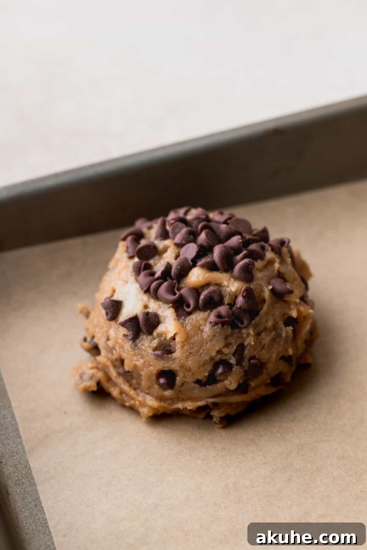 Perfectly scooped cookie dough balls with extra chocolate chips on a parchment-lined cookie sheet.