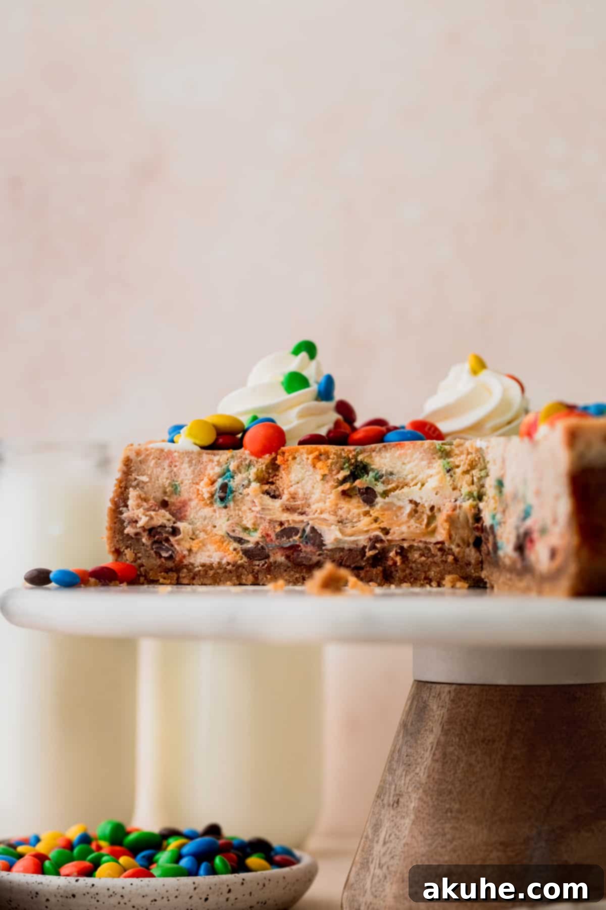 MM Cheesecake Bliss 2 M&M cheesecake on a cake stand cut into slices, revealing colorful M&Ms.