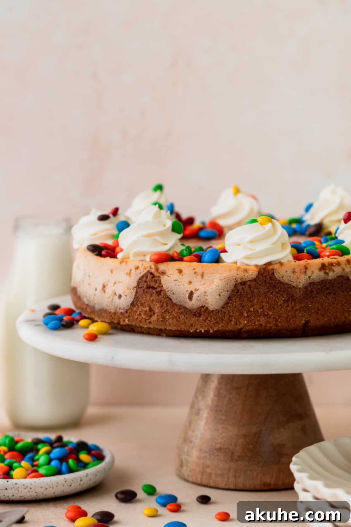 MM Cheesecake Bliss 9 A fully decorated M&M cheesecake on a cake stand, ready to be served.