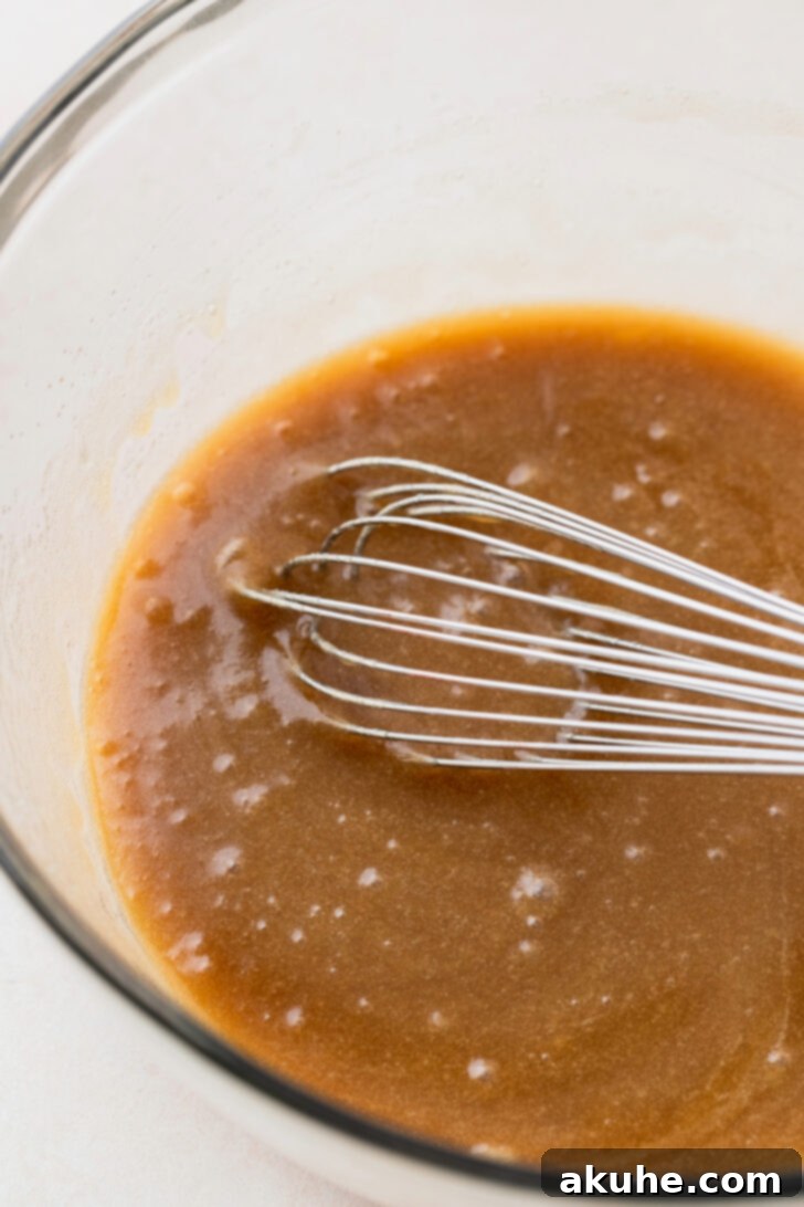 Java Delights 4 Wet ingredients (melted butter, sugars, vanilla, eggs) being mixed in a bowl.