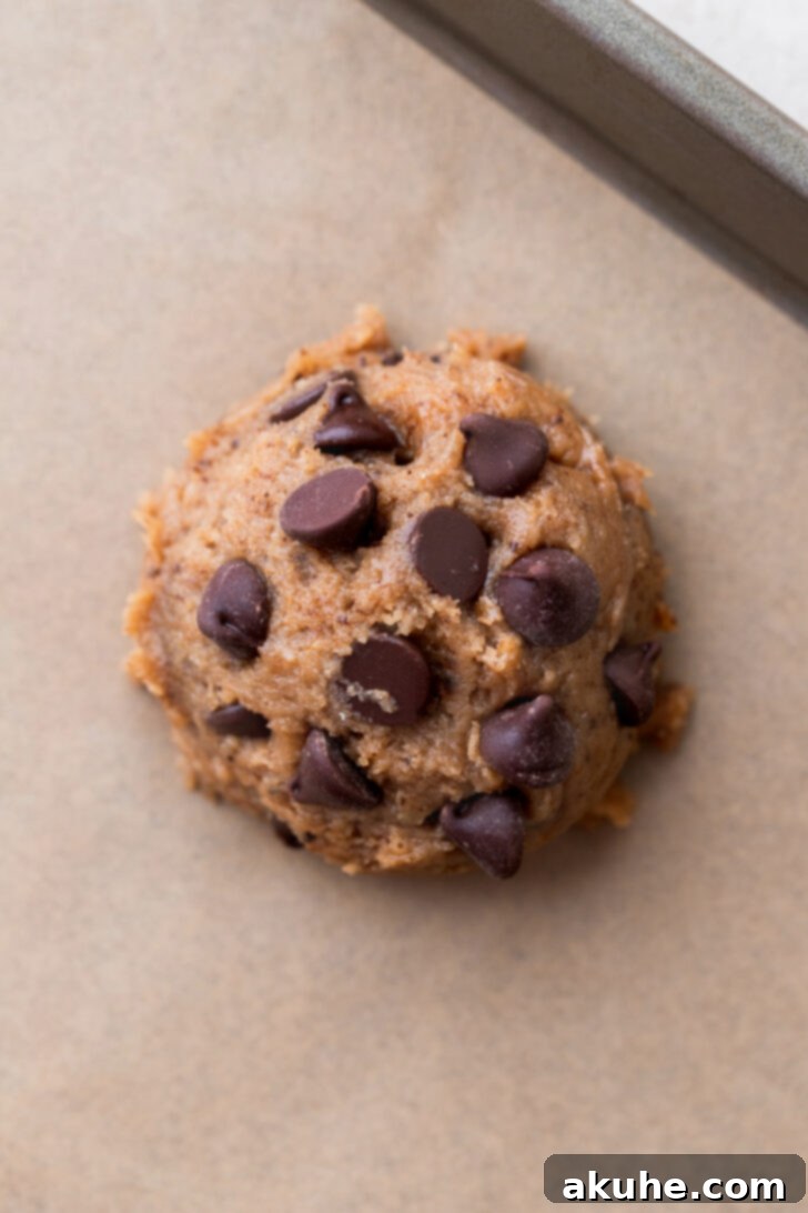 Java Delights 6 A scooped cookie dough ball topped with extra chocolate chips on a parchment-lined cookie sheet.