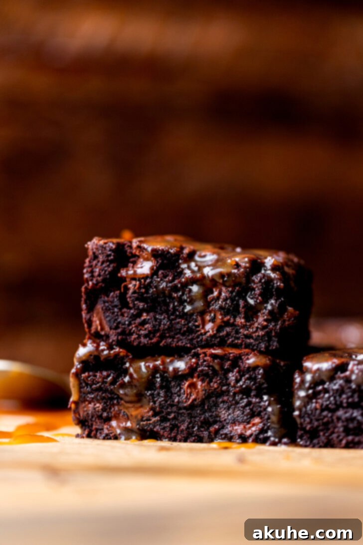 Close-up side view of two perfectly cut salted caramel brownies, showcasing the gooey caramel layer.