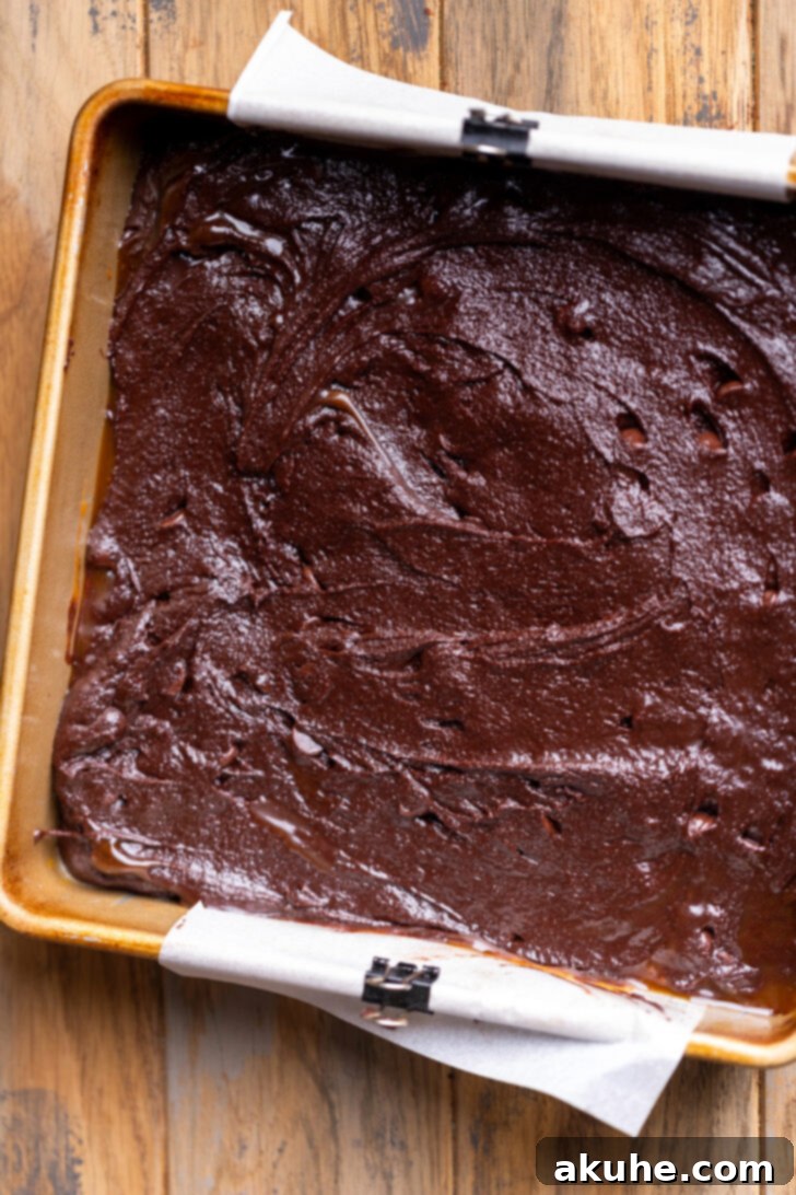 A baking pan filled with two layers of brownie batter, with a caramel layer sandwiched in between.