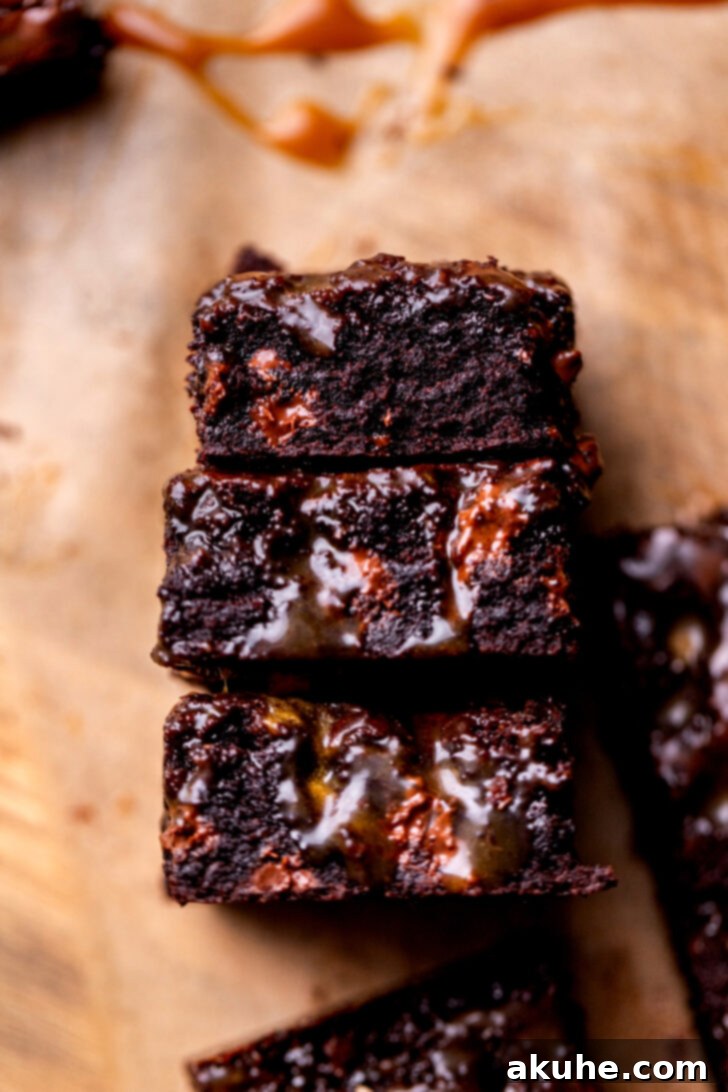 A stack of three rich salted caramel brownies, revealing their dense, fudgy texture and caramel swirls.