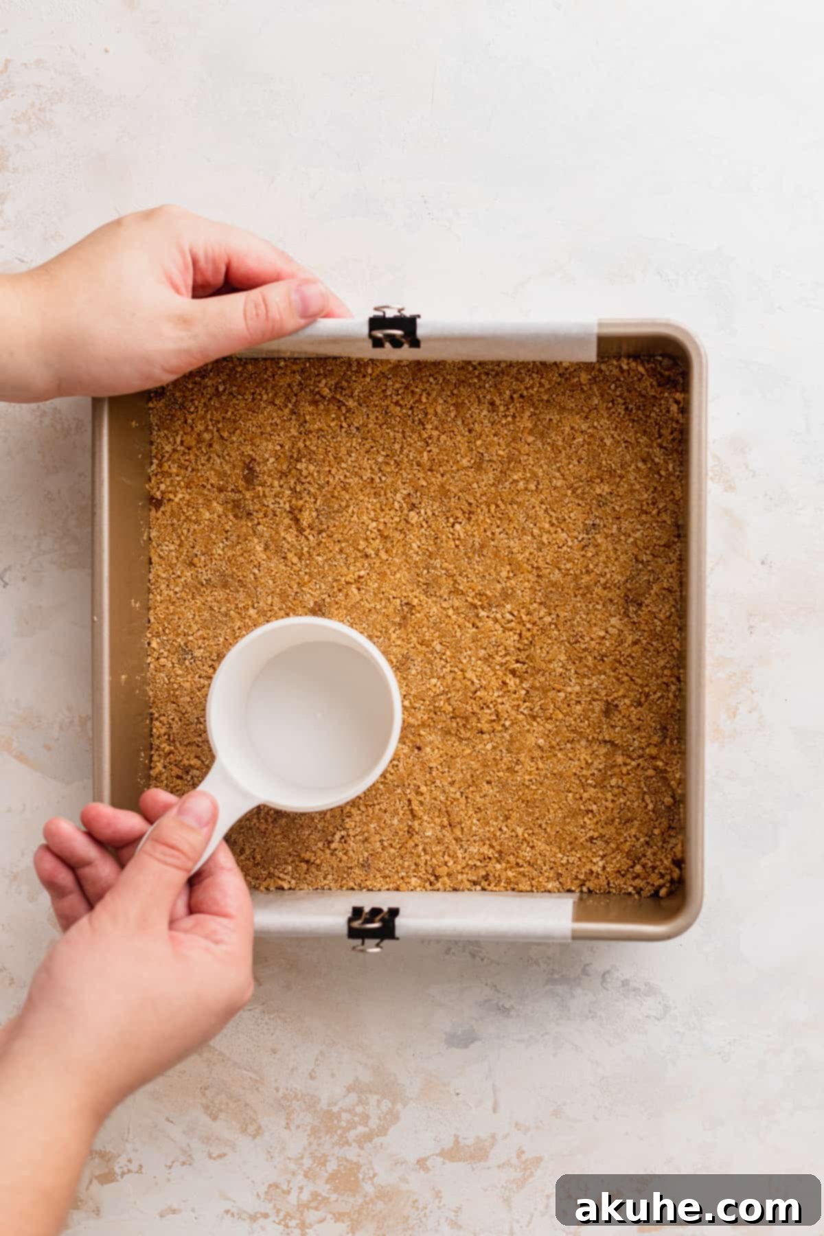 Decadent Cookie Dough Cheesecake Bars 6 Graham cracker crust being firmly compacted into a baking pan using the bottom of a measuring cup.
