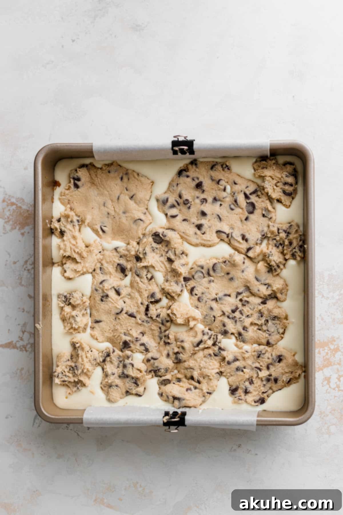 Decadent Cookie Dough Cheesecake Bars 8 Numerous small discs of chocolate chip cookie dough neatly placed on top of the cheesecake batter in a baking pan, ready for baking.