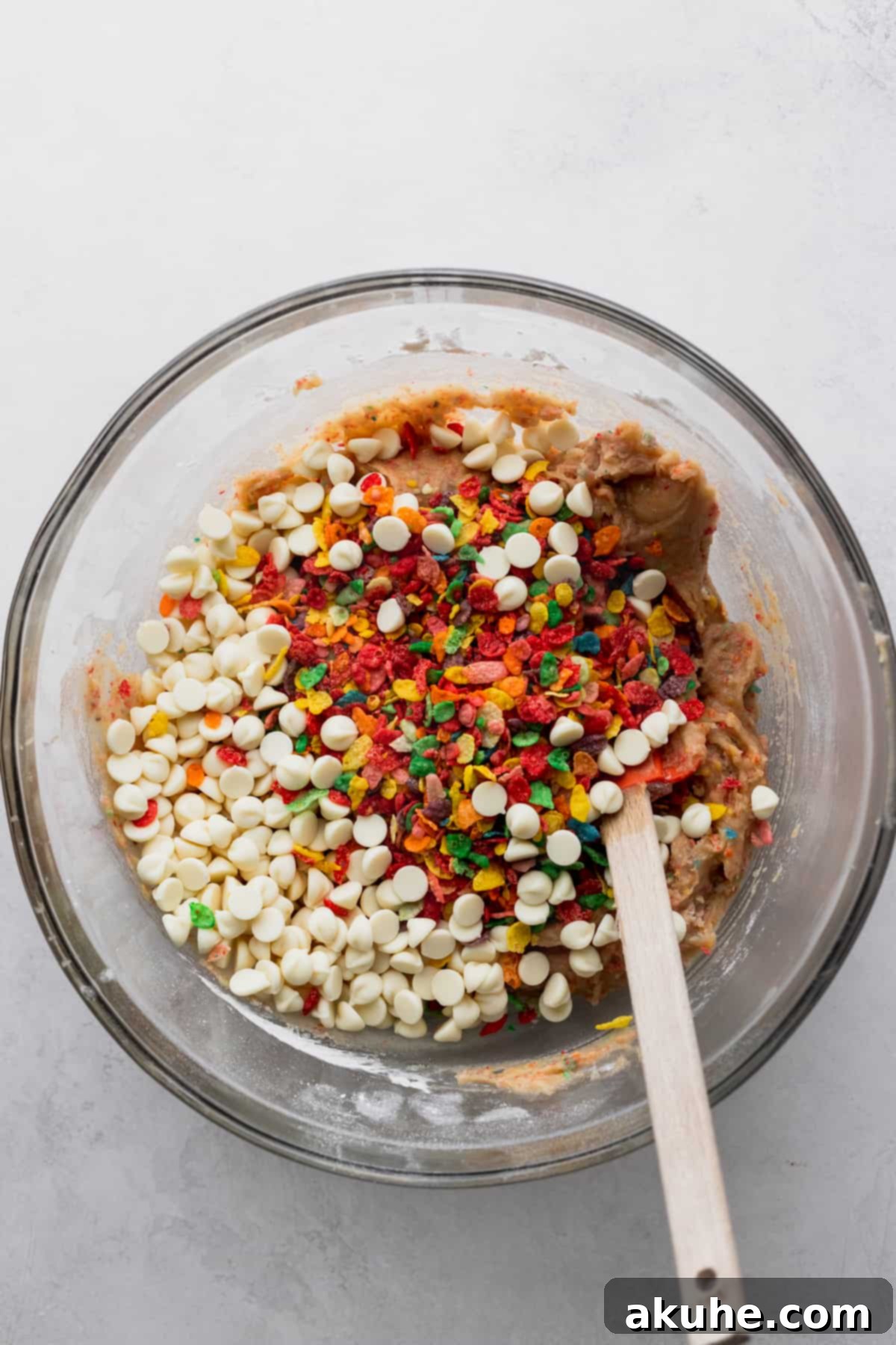 Fruity Pebbles Cookies 5 Cookie dough in a glass bowl with colorful Fruity Pebbles cereal and white chocolate chips folded in.