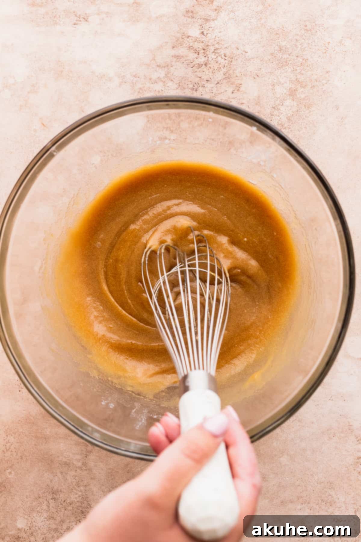 Warm Cocoa Blossom Cookies 4 Mixing wet ingredients in a clear glass bowl with a whisk, showing a smooth, golden-brown mixture.