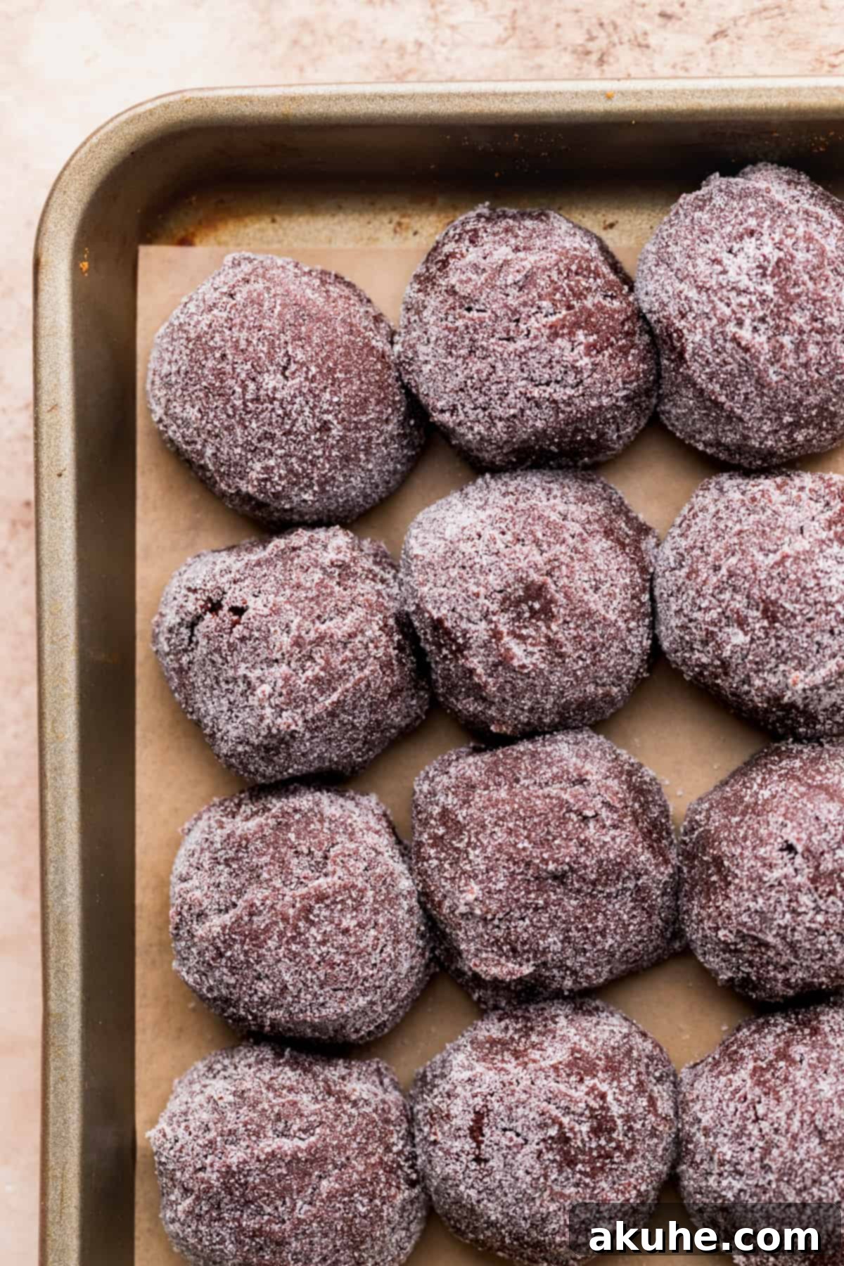 Warm Cocoa Blossom Cookies 7 Rows of chocolate cookie dough balls, generously coated in white sugar, neatly arranged on a parchment-lined cookie sheet, ready for baking.