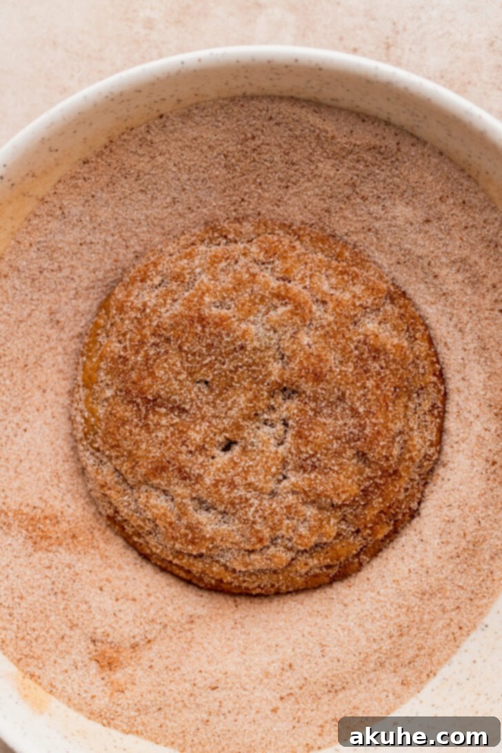 A baked cookie being generously coated in cinnamon sugar.