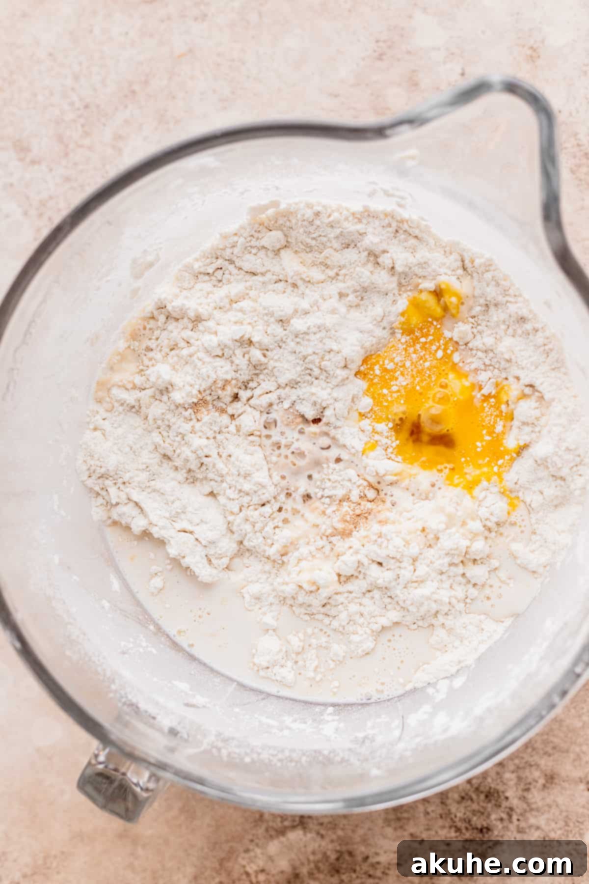 Decadent Caramel Cinnamon Rolls 5 Wet ingredients (milk and eggs) being added to the dry flour and butter mixture in a bowl.