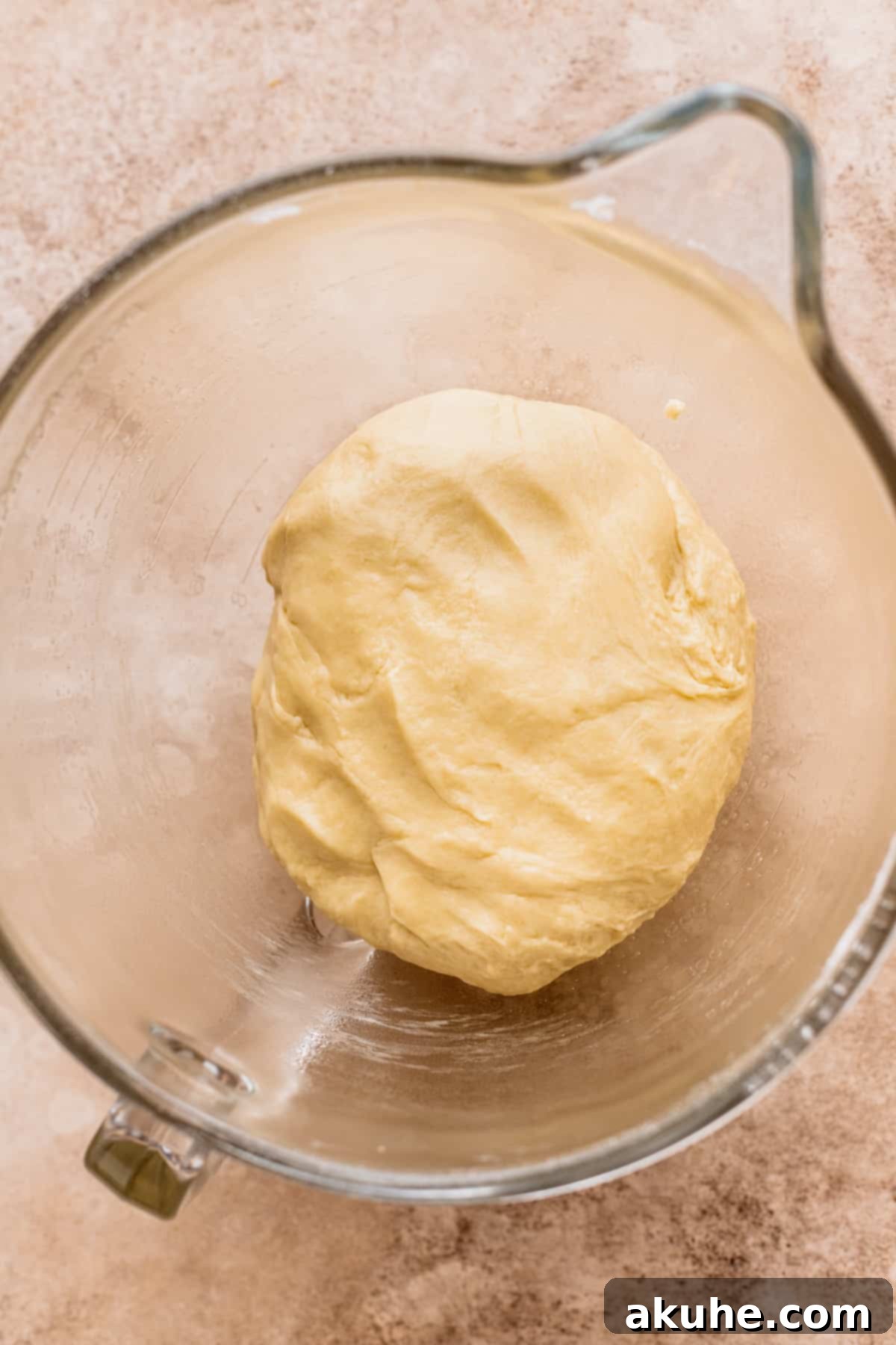 Decadent Caramel Cinnamon Rolls 6 Dough resting in a glass bowl before its first rise, covered with a kitchen towel.