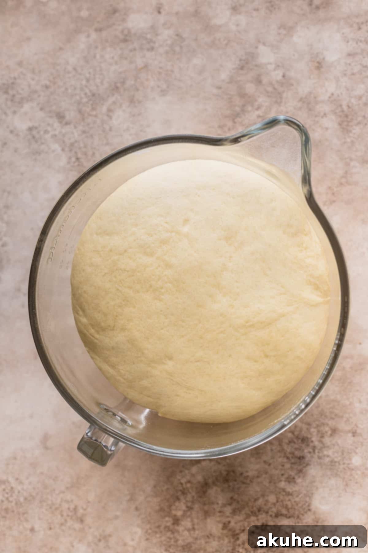 Decadent Caramel Cinnamon Rolls 7 Well-risen dough in a glass bowl, significantly expanded after proofing.