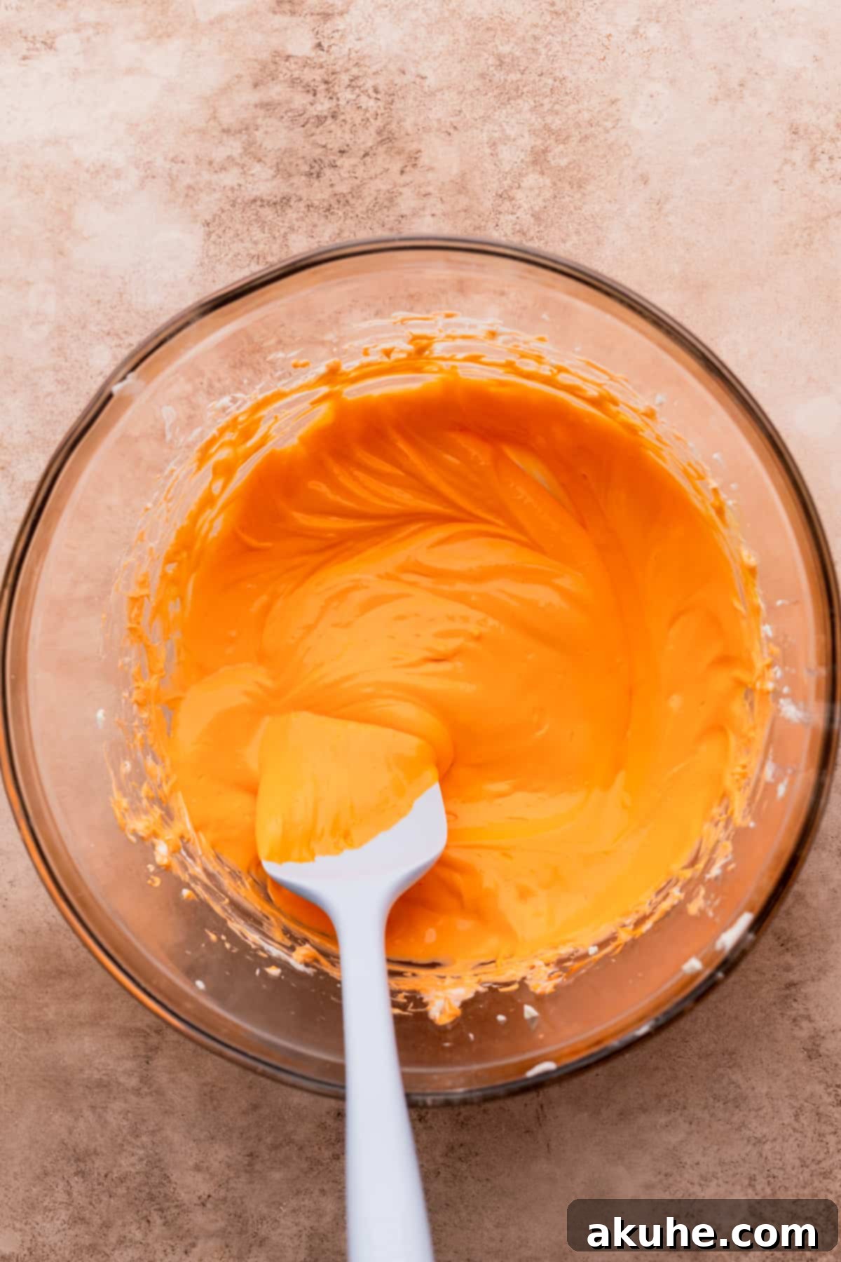Orange-tinted cream cheese mixture in a glass bowl, ready for layering.