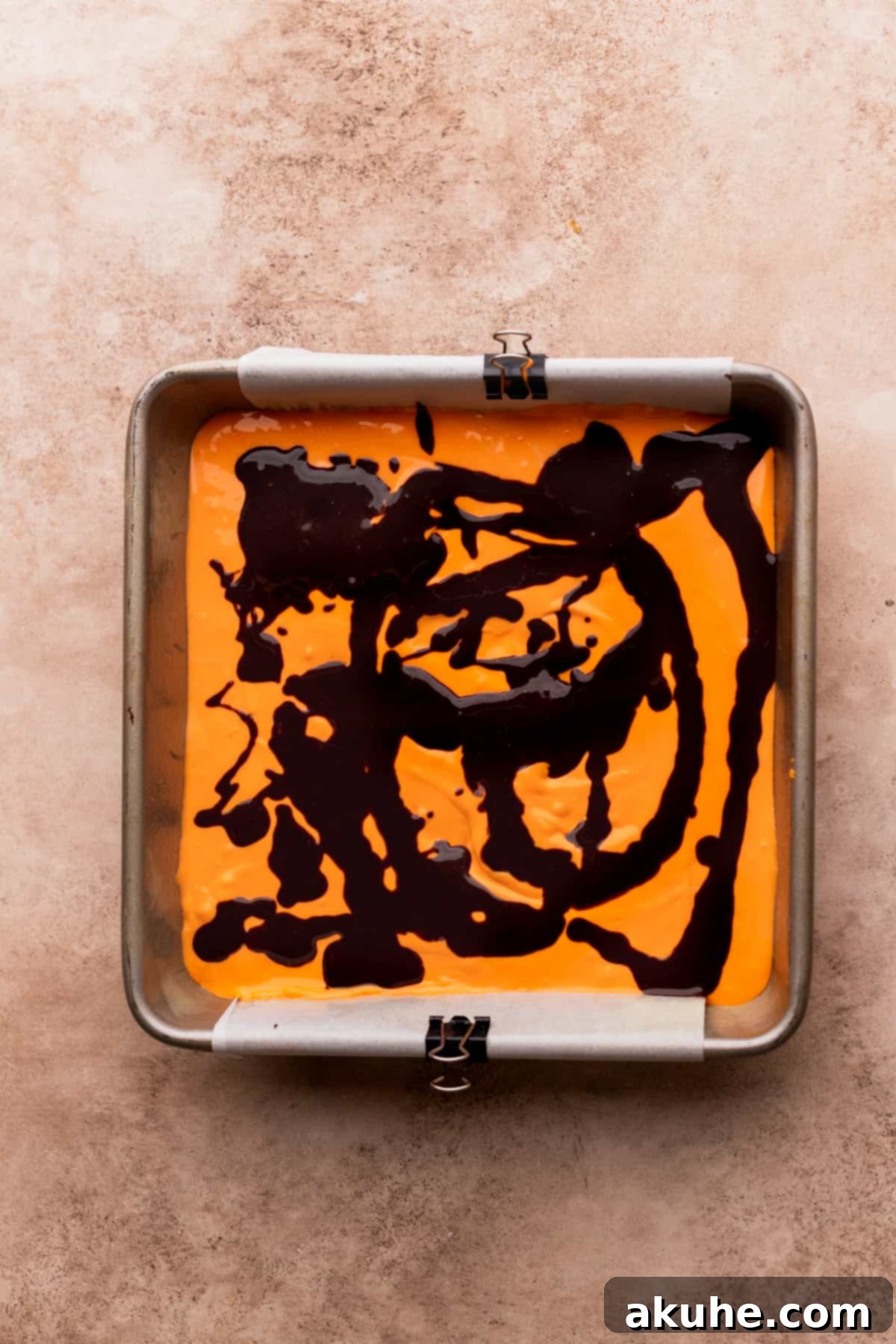 Thinned brownie batter drizzled over the orange cheesecake layer.