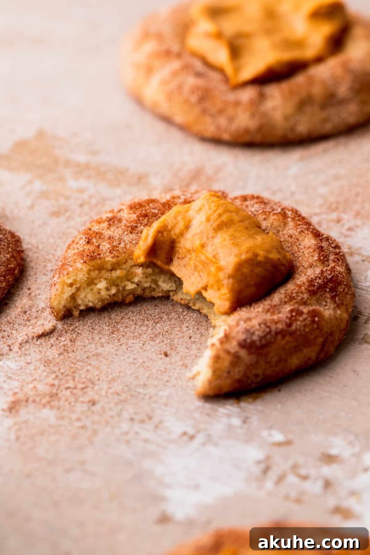 A baked pumpkin pie cookie with a bite taken out, showing the creamy pumpkin cheesecake filling inside.