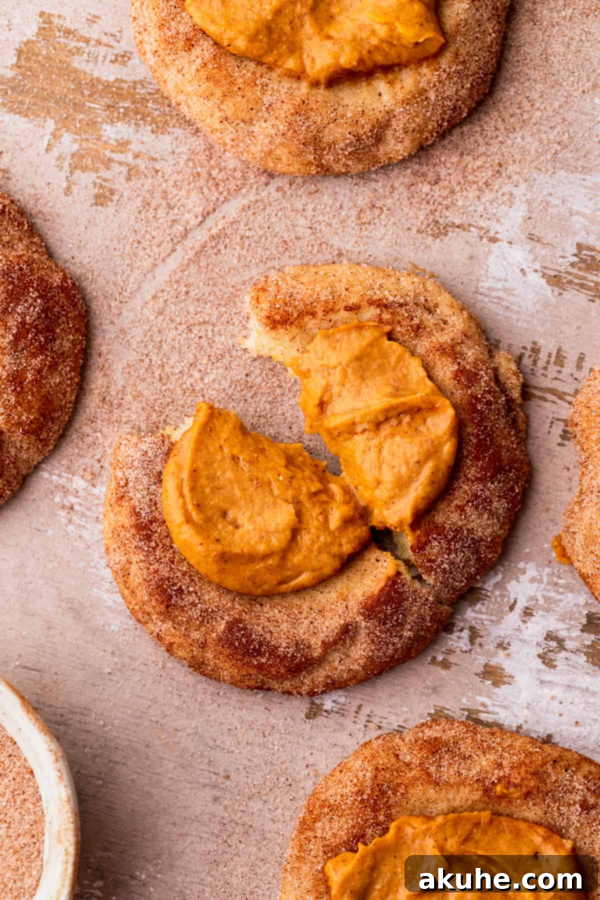 A freshly baked pumpkin pie cookie split in half, revealing its soft snickerdoodle exterior and creamy pumpkin cheesecake filling.
