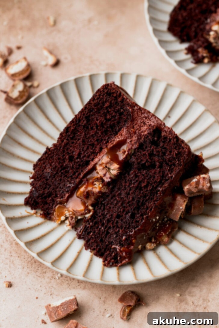 Ultimate Twix Cake 2 Slice of twix cake on a plate, showcasing its layers of chocolate cake, salted caramel, and Twix pieces.