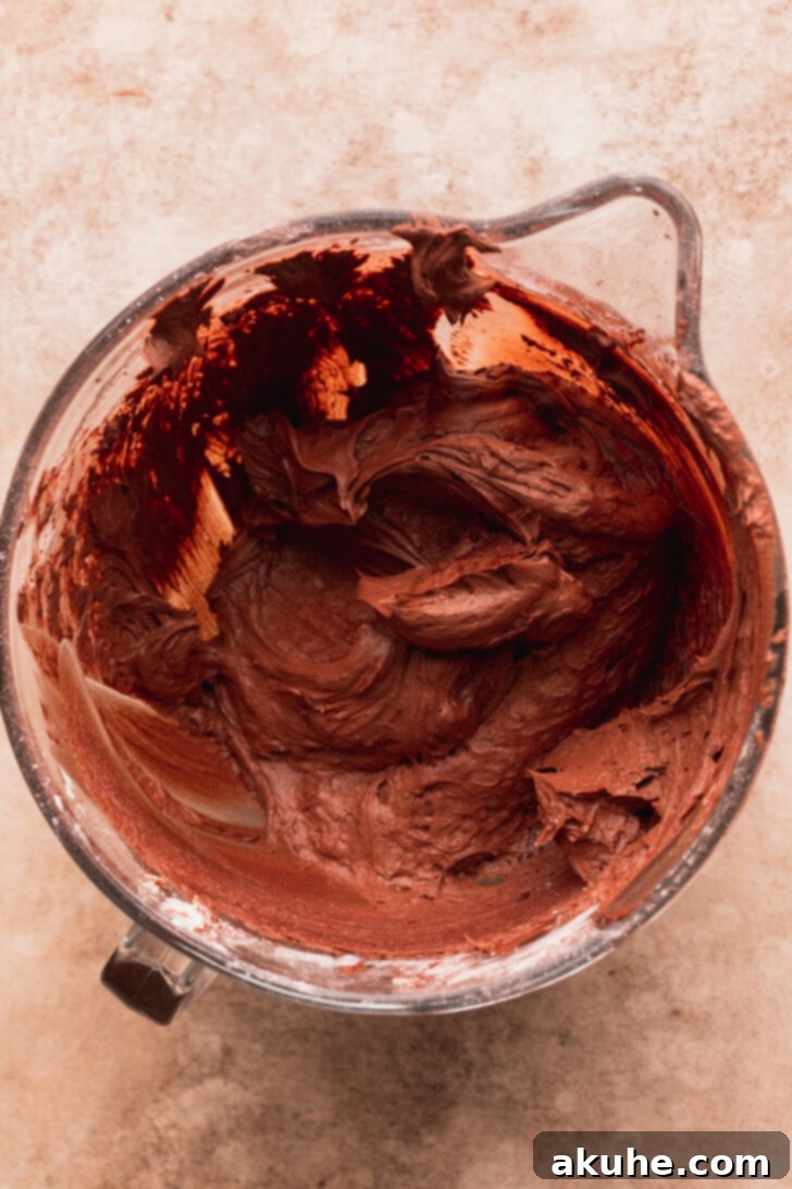 Ultimate Twix Cake 6 Smooth chocolate cream cheese frosting in a glass bowl with a spatula.