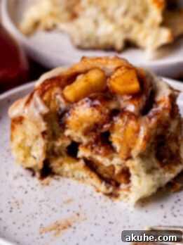 Homemade Apple Cinnamon Rolls 11 A delightful apple cinnamon roll on a plate with a bite taken out, showcasing its soft interior and rich filling.