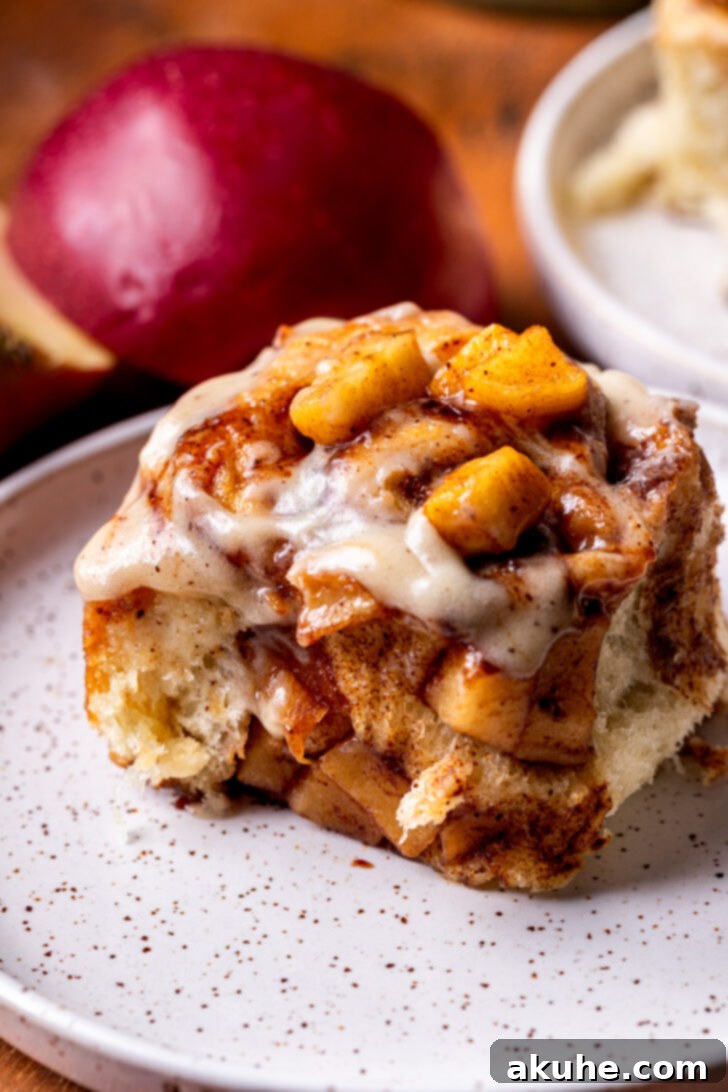 Homemade Apple Cinnamon Rolls 9 A single apple cinnamon roll on a white plate, showcasing its soft layers and generous icing.