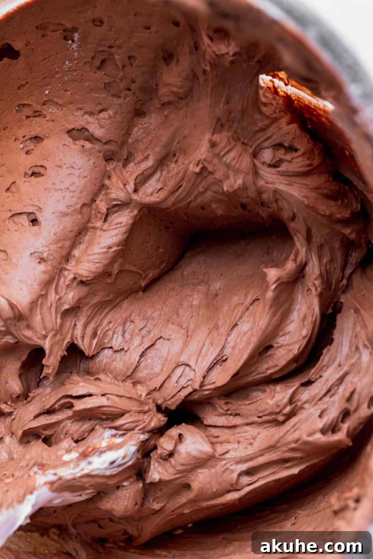 Silky smooth chocolate frosting in a clear glass bowl, perfectly whipped and ready to adorn the cake with its rich, dark color.