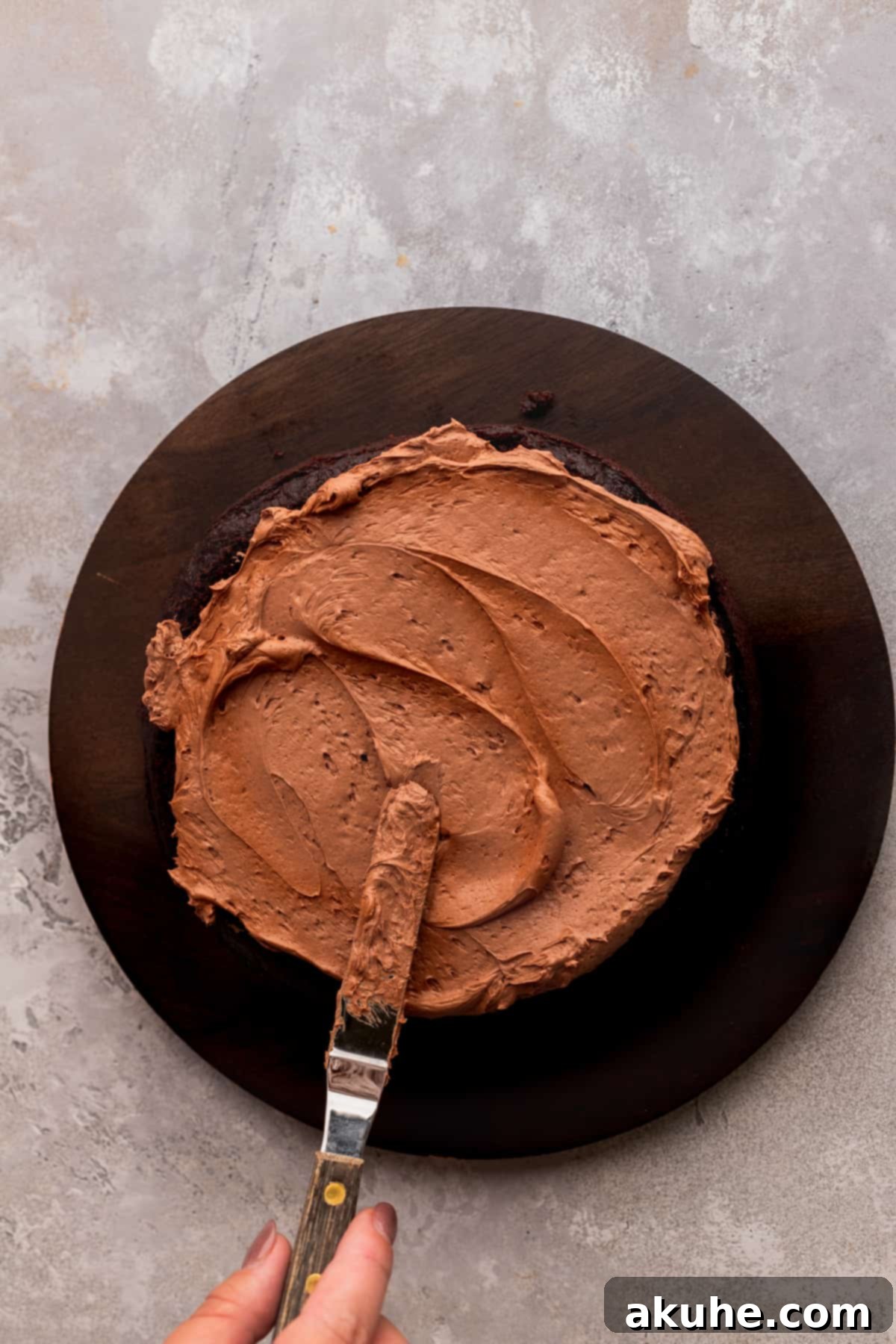 Expertly spreading rich chocolate frosting onto the top layer of the cake, preparing for a flawless, smooth finish.