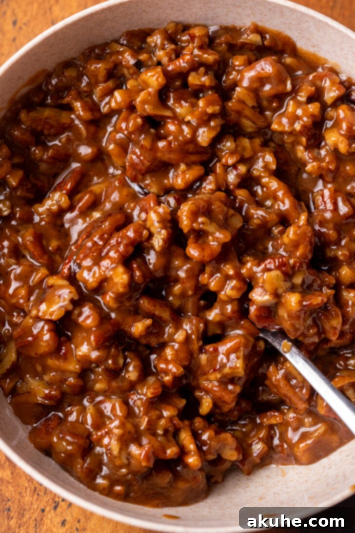 A bowl of rich, amber-colored pecan pie filling with whole and chopped pecans visible.