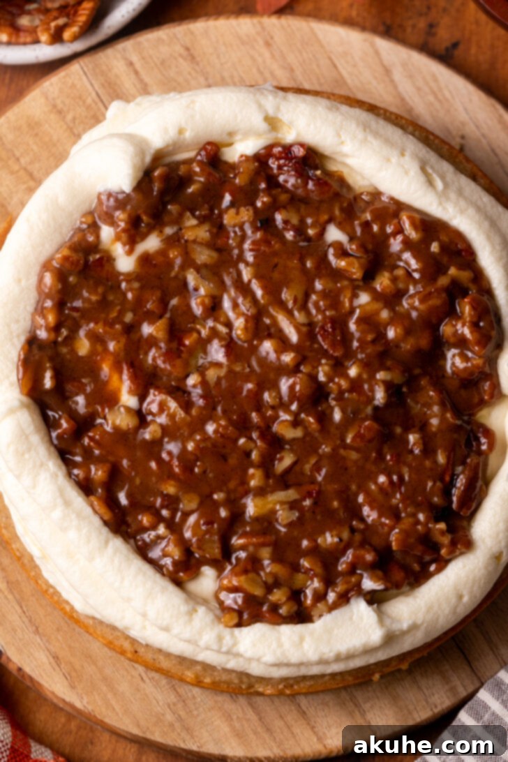 A layer of spice cake topped with a spread of cream cheese frosting, a piped frosting border, and a generous layer of pecan pie filling.
