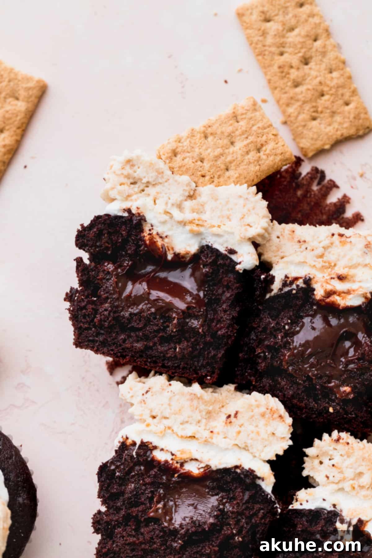 Two S'mores cupcakes, one sliced in half to showcase the rich chocolate ganache filling and the layers of marshmallow and frosting.