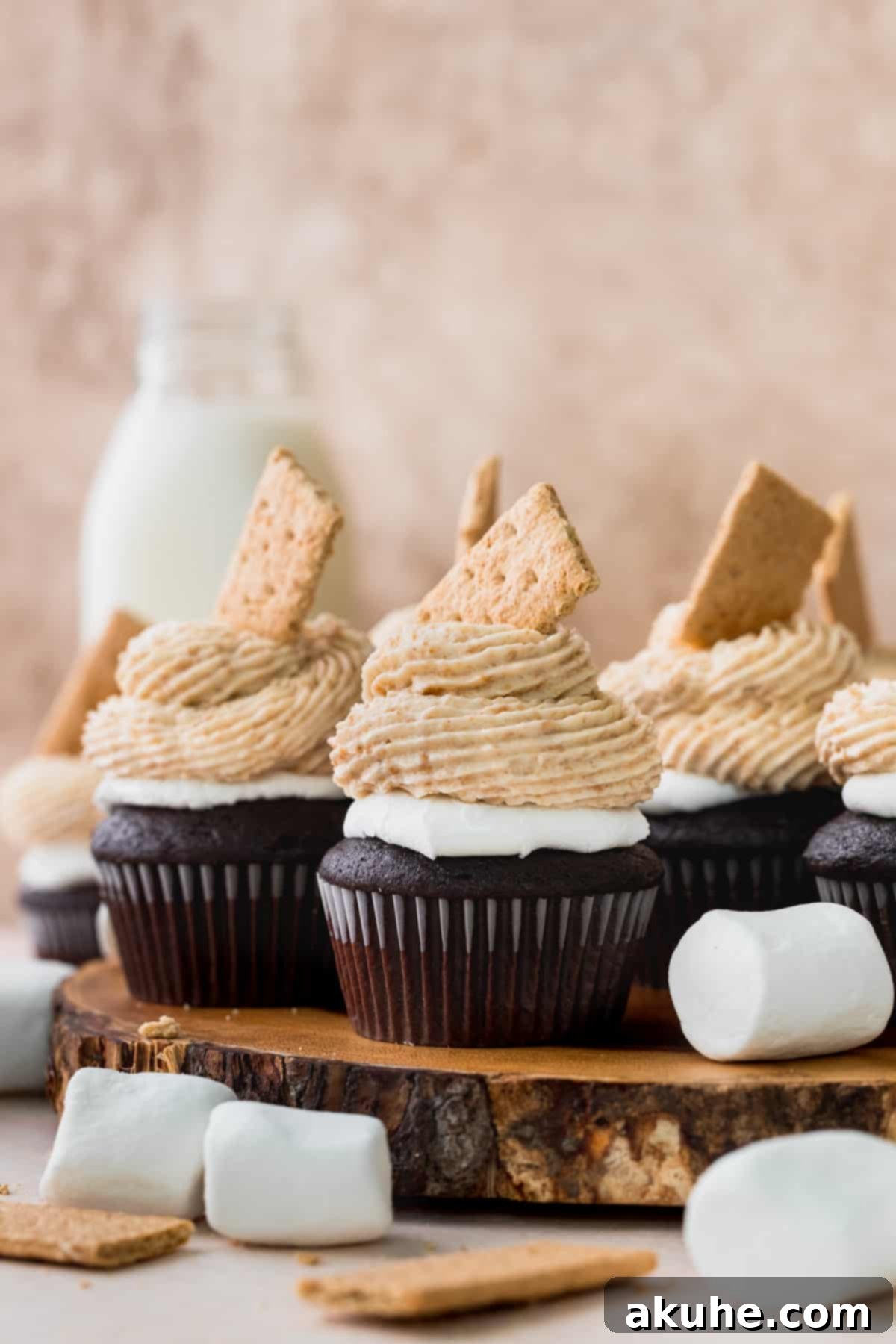 A close-up shot of several S'mores cupcakes, beautifully decorated and arranged on a rustic wooden board, showcasing their toasted marshmallow and frosted tops.