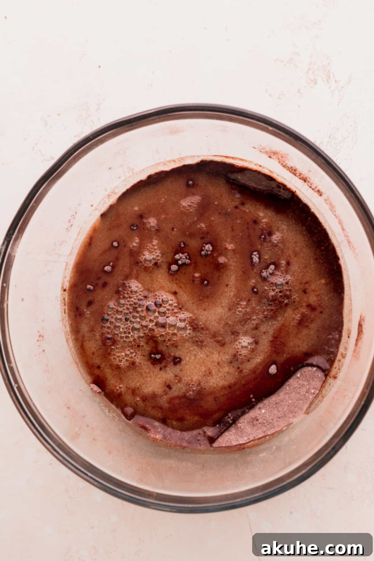 The wet ingredients being gently poured over the dry ingredients in a large glass bowl, illustrating the initial mixing stage.