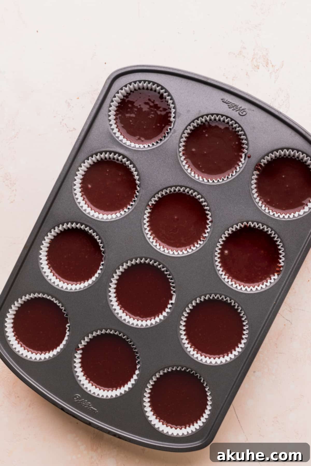 Chocolate cake batter perfectly portioned into cupcake liners within a cupcake pan, ready for the oven.