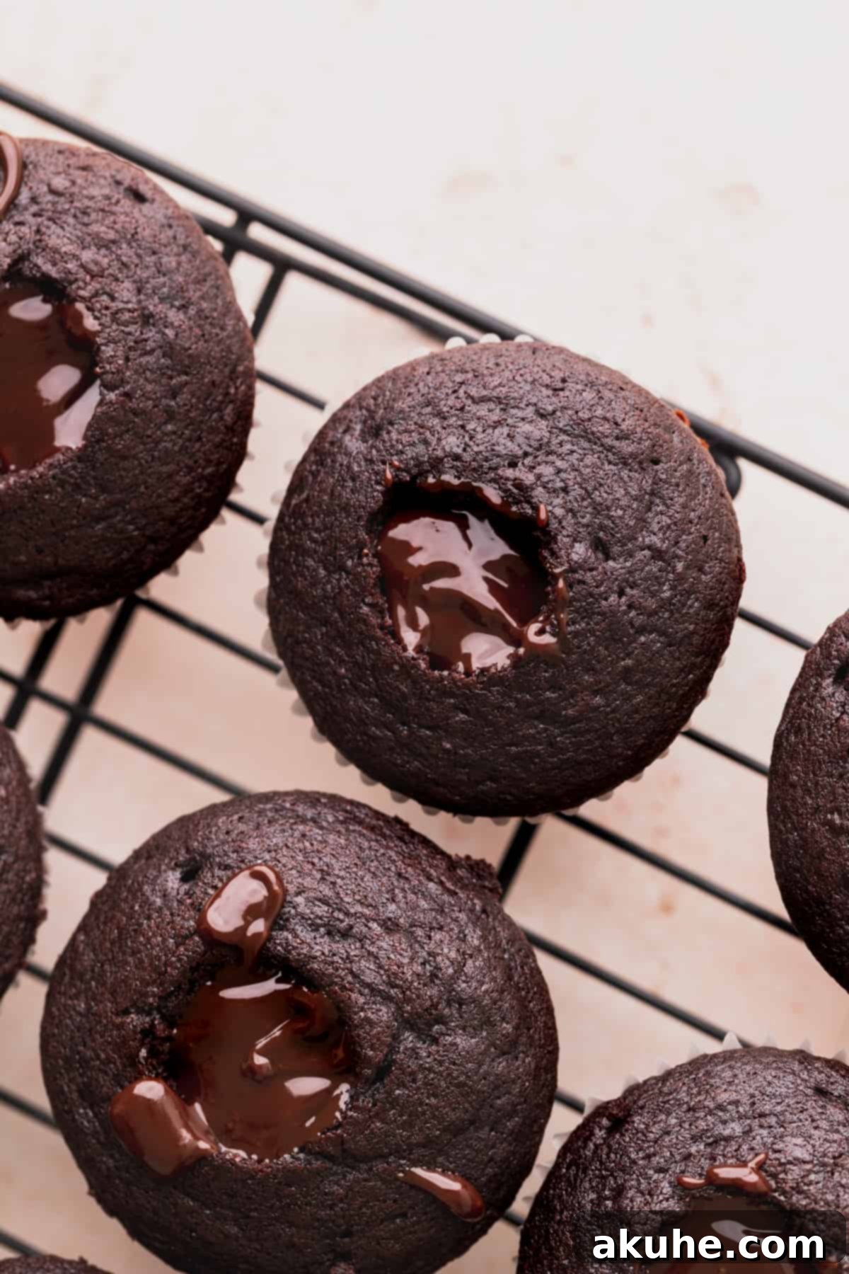 Cupcakes meticulously cored and filled with rich chocolate ganache, sitting on a wire rack.