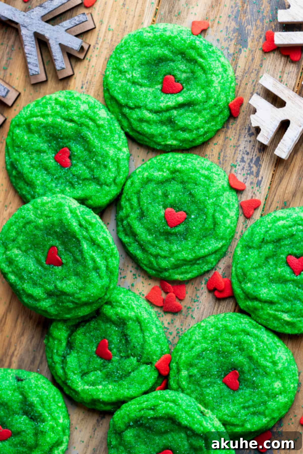 Grinch cookies artfully spread out on a rustic wooden board, showcasing their vibrant green color and heart sprinkles.