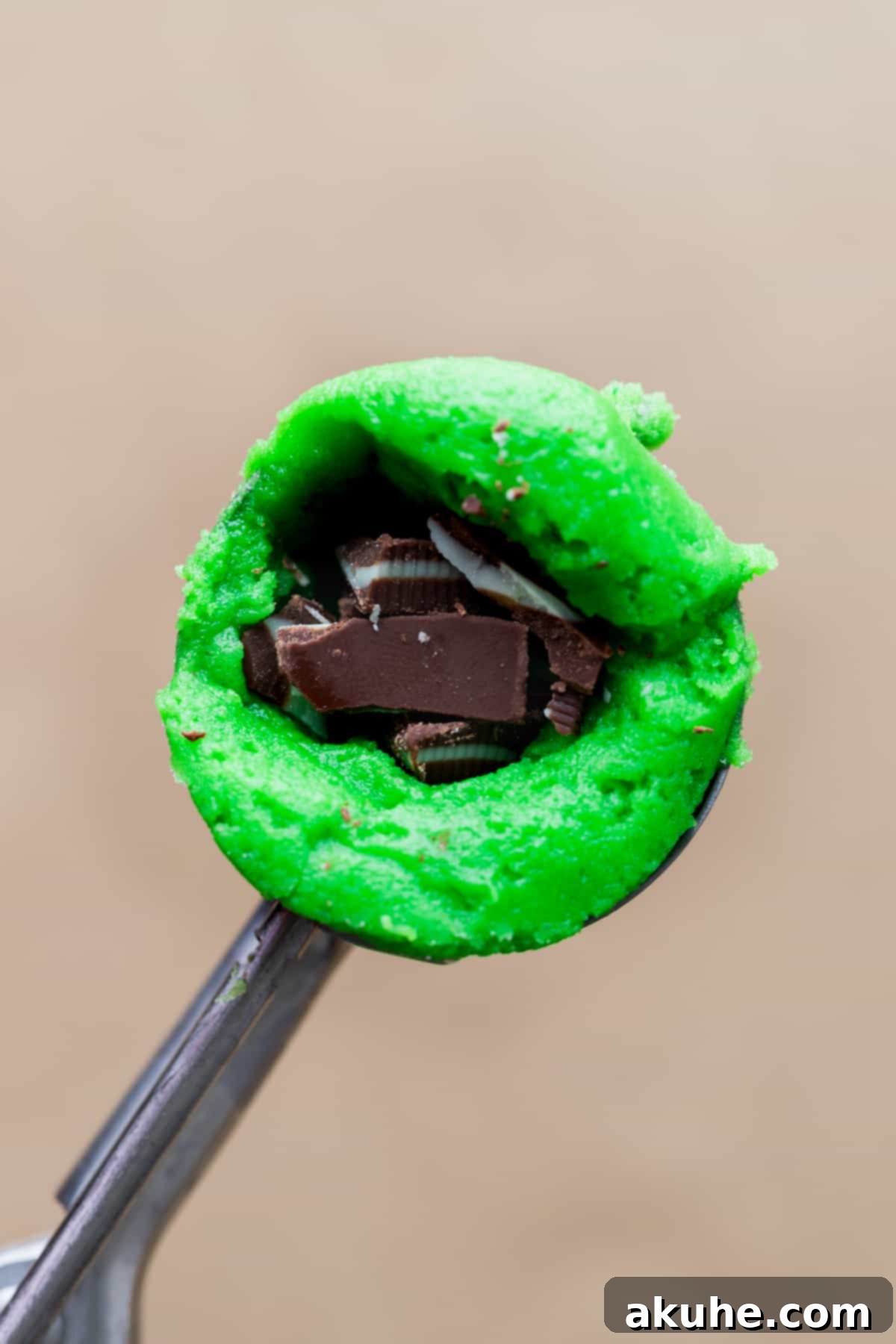 Green cookie dough ball in a scoop with a thumb-pressed hole, being filled with chopped Andes mints.