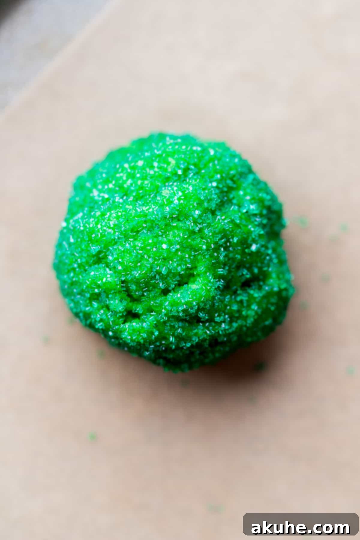 A green sugar-coated cookie dough ball resting on parchment paper, ready for baking.