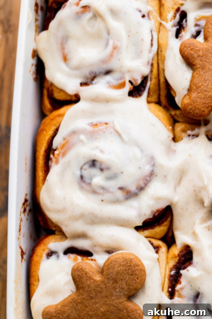 Spiced Gingerbread Swirl Buns 9 A stunning top-down view of a pan of warm gingerbread cinnamon rolls, glistening with brown butter cream cheese icing.